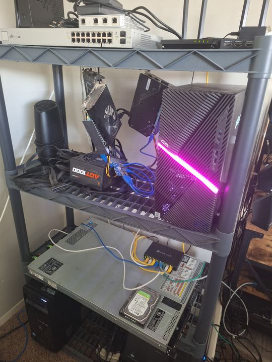 The homelab rack in mid-2025: UniFi switch on top, a Dell G5 glowing pink, the PowerEdge R620 and TP-Link switch below.